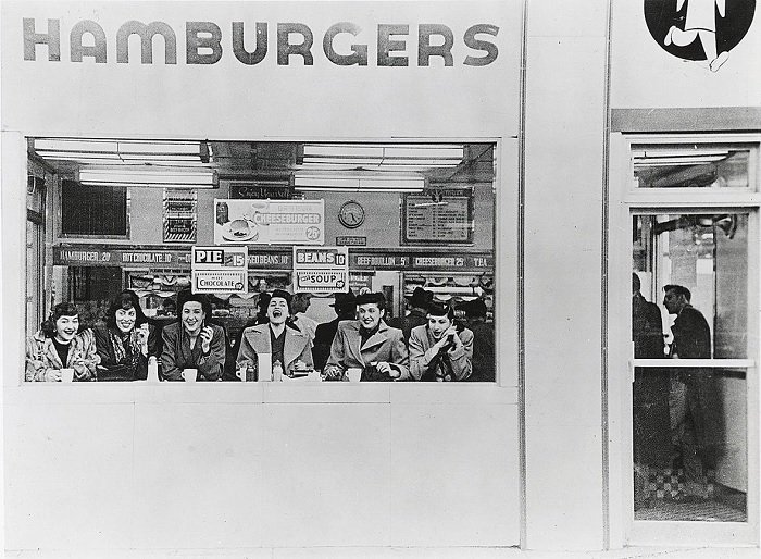 Six women sitting in the window of a hamburger store