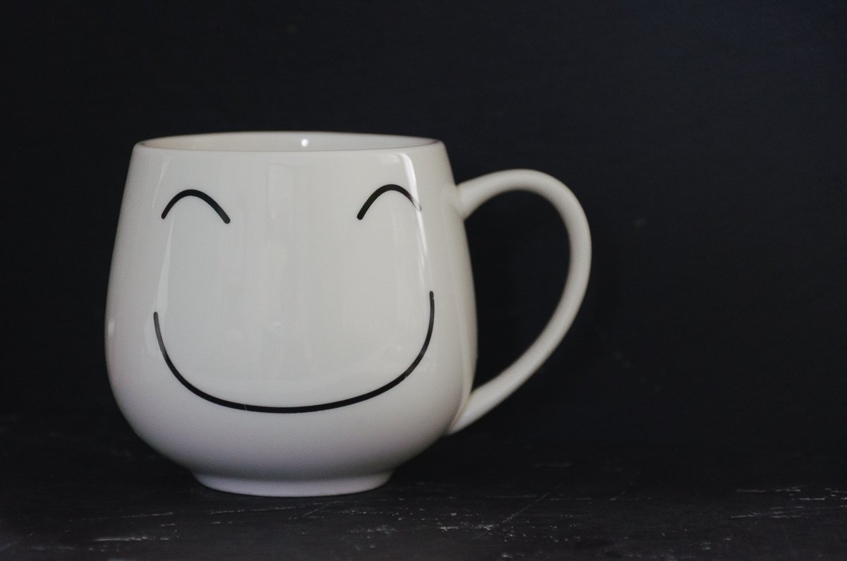 A white mug with a happy face on it against a black background