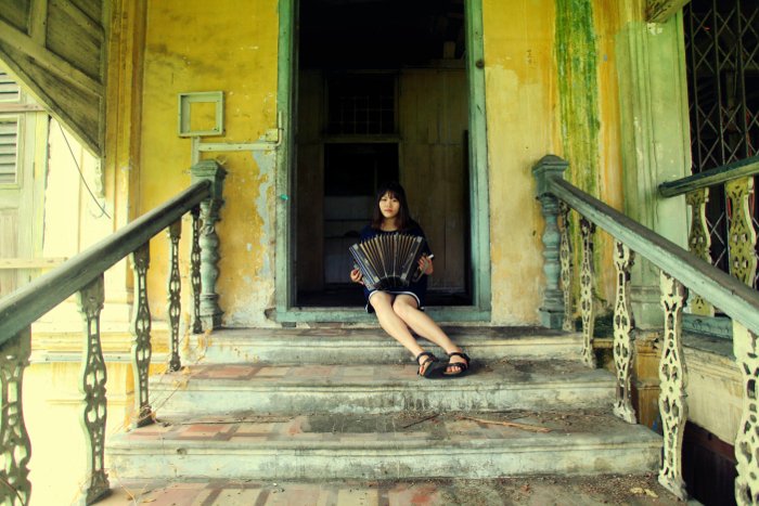 Photo of a girl playing the accordion on the stairs of an abandoned house