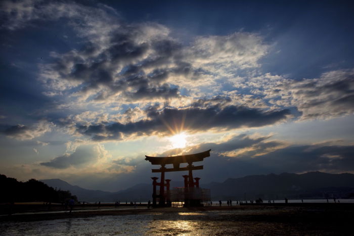 Photo of an Asian-style gate with blue sky, clouds, and the sun shining through