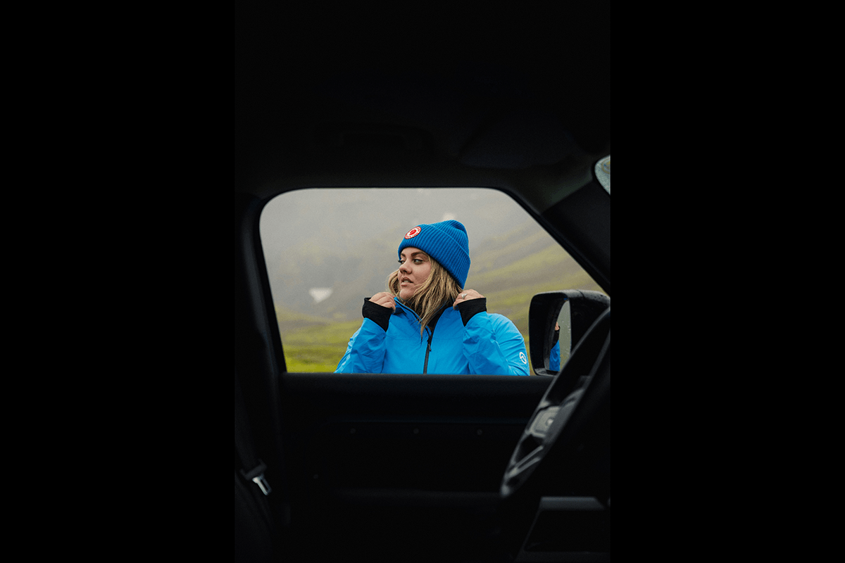 A woman in a blue beanie and coat seen through a window of a dark car interior as a way of framing photography shots