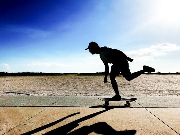 Photo of a skateboarding man in movement with blue sky background