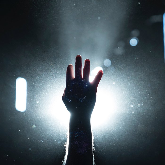 Photo of a hand reaching up with sharp light in the background