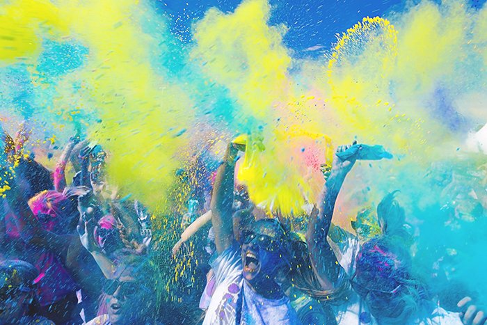 Photo of a crowd at a festival with yellow and blue color powder thrown in the air