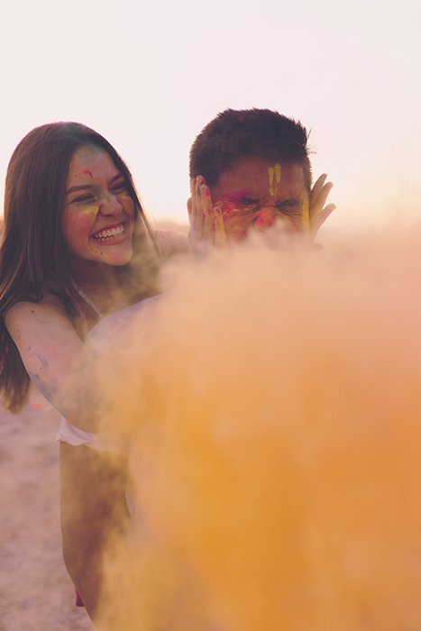 Photo of a girl and a boy with simple background behind yellow color powder
