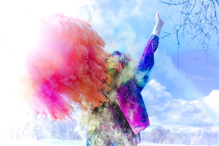 Photo of a man in colored jacket with a cloud of orange powder in front of him