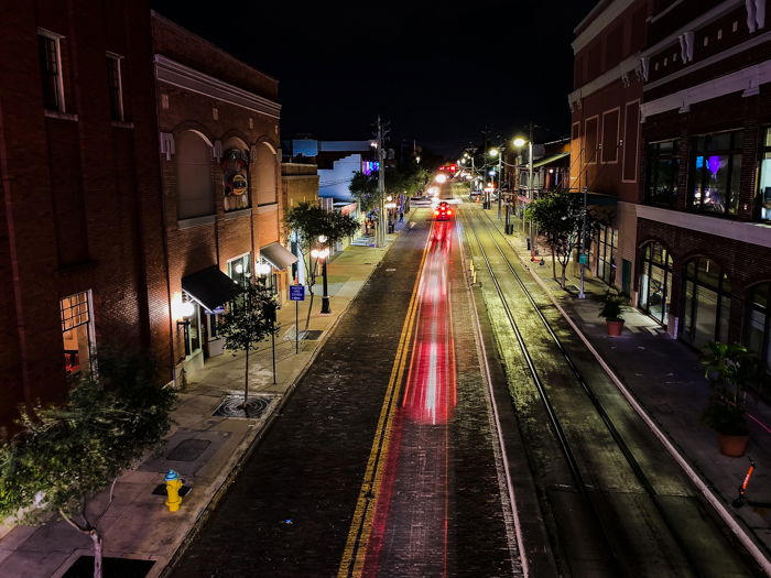 A long-exposure of a street at night with some streaks of red traffic light trails on a street with buildings on either side