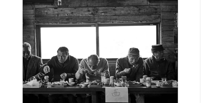 Black and white photo of older man eating at a table by Gentl & Hyers