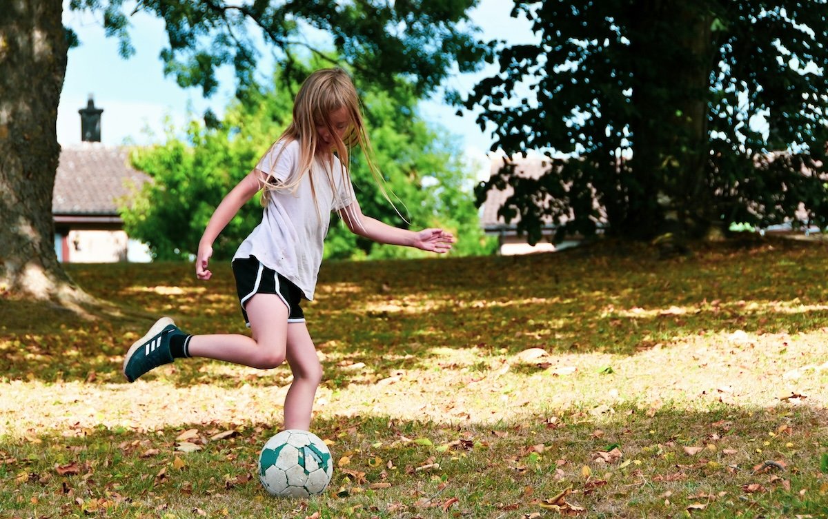 A girl kicking a soccer ball taken with sports photography equipment