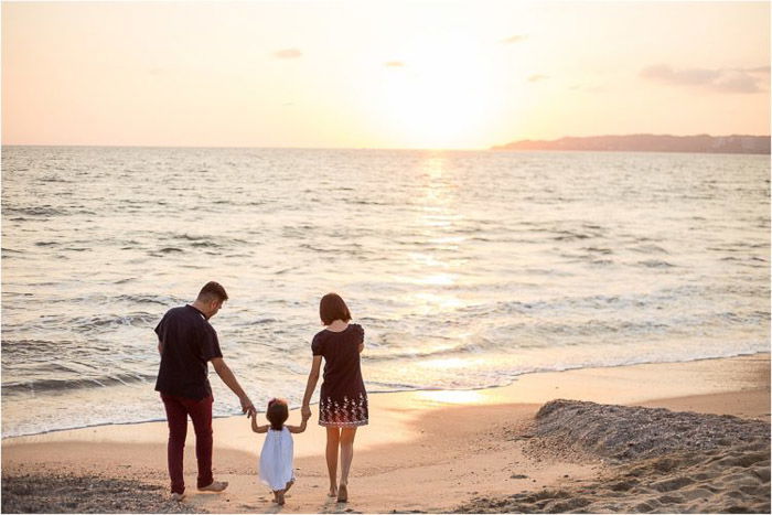 sweet family portrait of parents holding a little girls hand outdoors on the beach