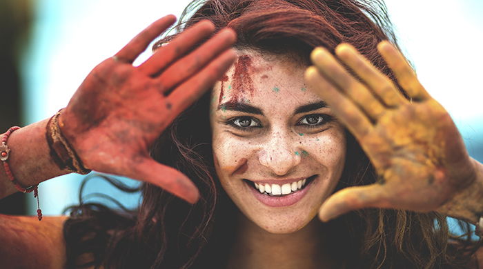 Young woman holding paint covered hands up to frame her face.