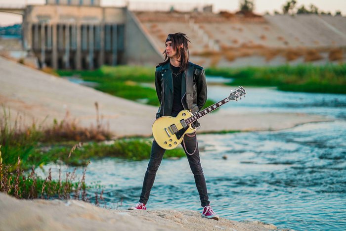 A guitarist standing in front of a river 