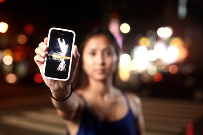 A woman holding a smartphone, the phone is in focus, while the rest of the image is blurred