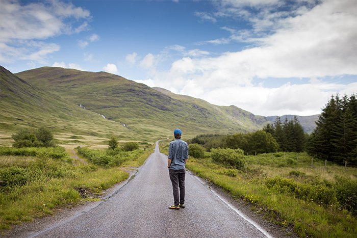 A landscape image with a man standing in the middle of a countryside road. 