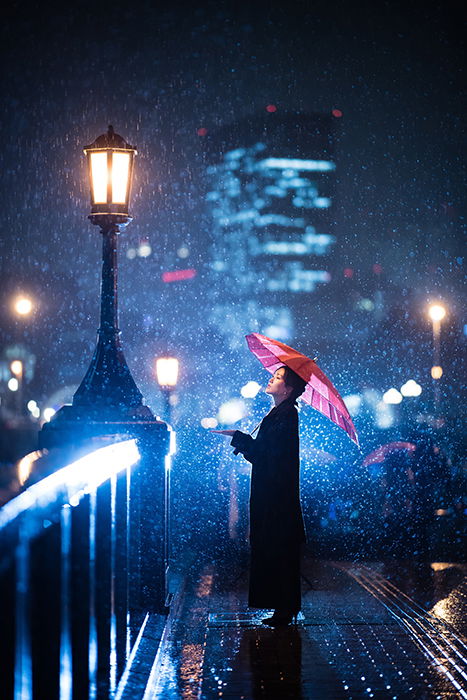 Photo of a woman standing under an umbrella in the snow with blue lights in the background