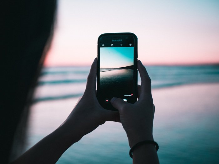 a girl taking a beach photo on a smartphone at sunset