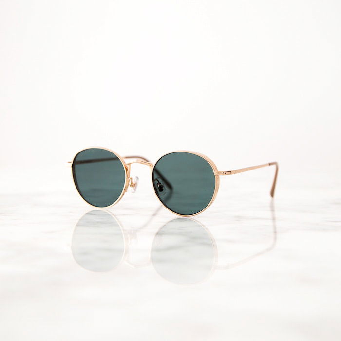 a pair of gold rimmed sunglasses on a reflective white surface 