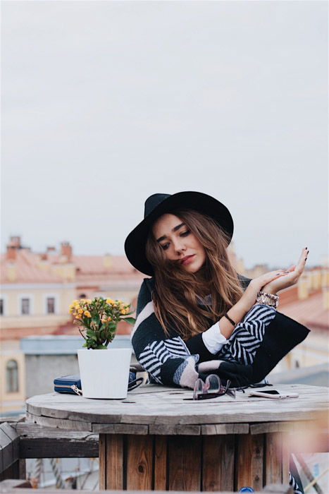 a stylish young woman sitting at a wooden table outdoors 