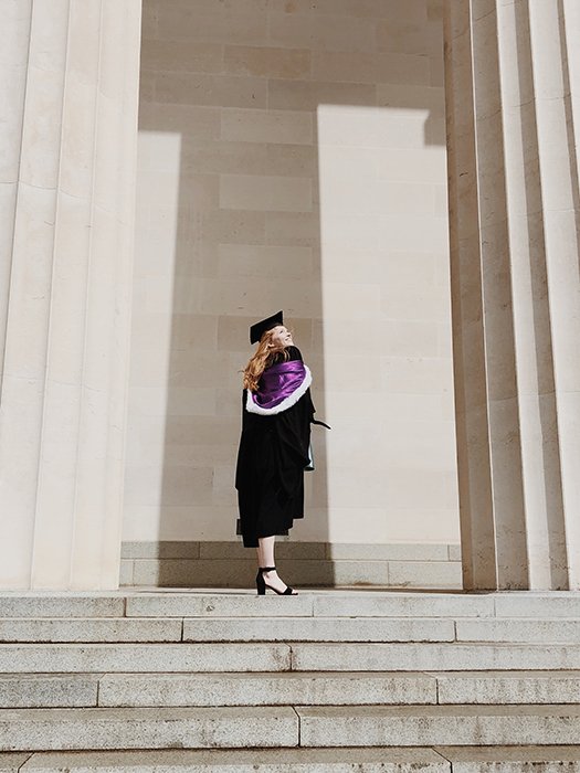 a student in graduation clothes posing on steps