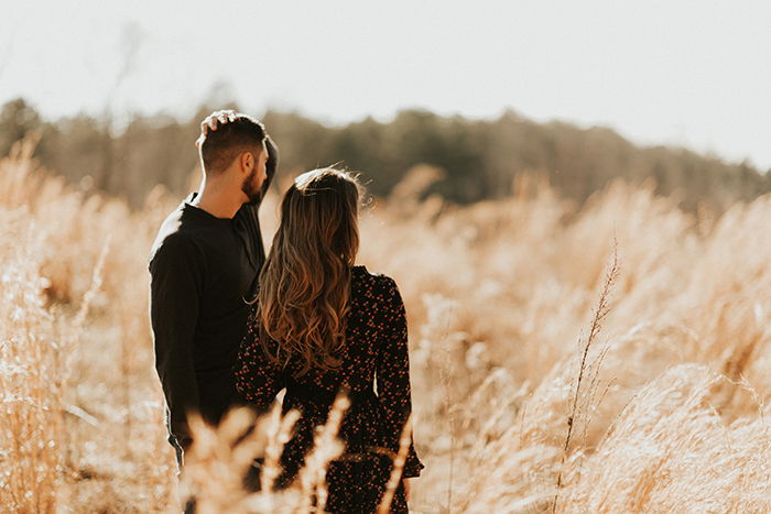 A couple posing outdoors, holding hands and looking in one direction together