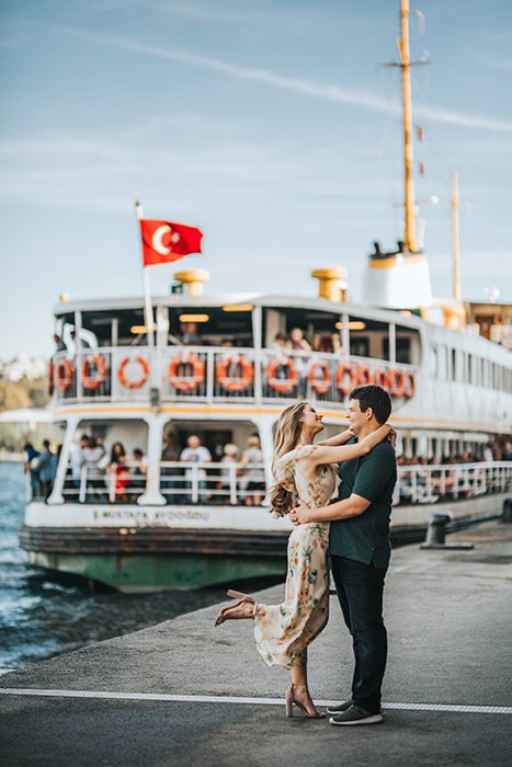 A couple embracing at a pier in front of a large boat