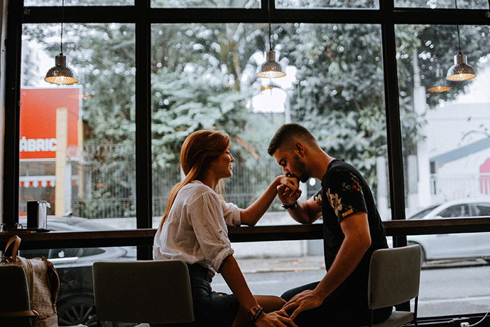 A man kissing his girlfriends hand in a cafe