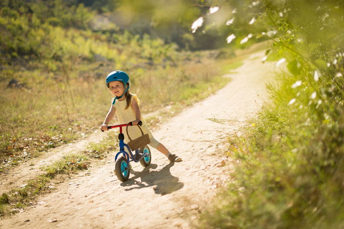 Photo of a little girl with a small bicycle on a dirt road