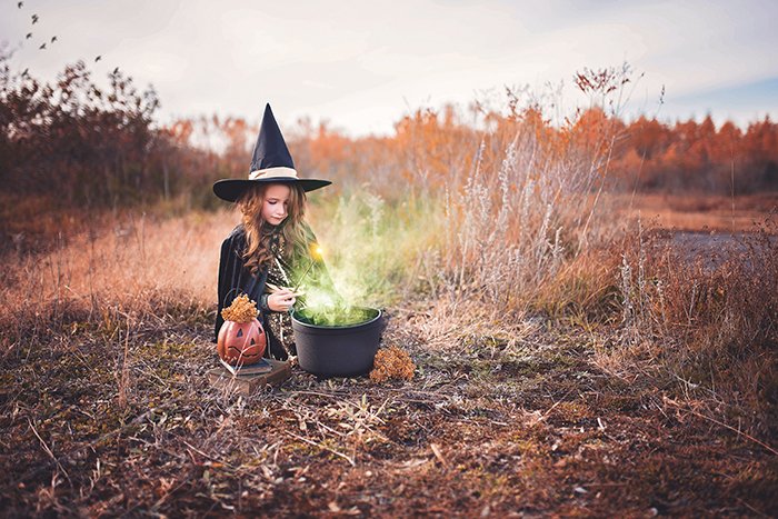 A little girl dressed as a witch. Her cauldron has been edited to look like there is a potion brewing inside it. 