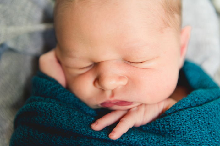 Close-up photo of a newborn baby swaddle in a turquoise blanket 