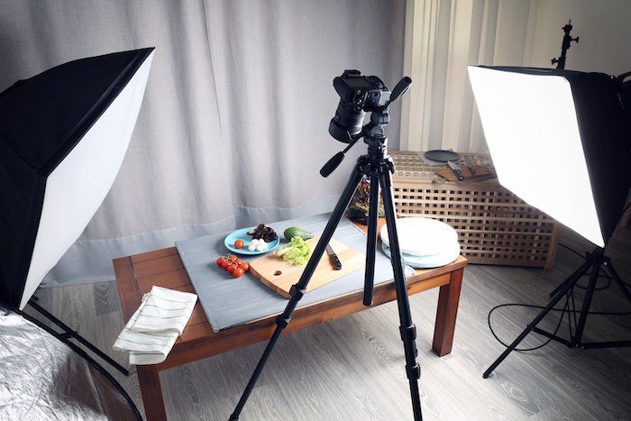 A tripod, camera, and lighting with soft boxes setup to shoot food on a coffee table in a living room