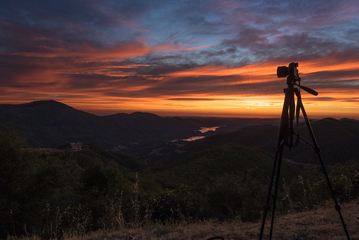A tripod and camera setup for a landscape photo of mountains and a valley at sunset
