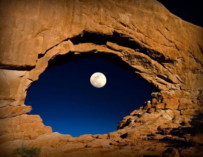 Photo of a cave with the moon appearing in a hole in the middle