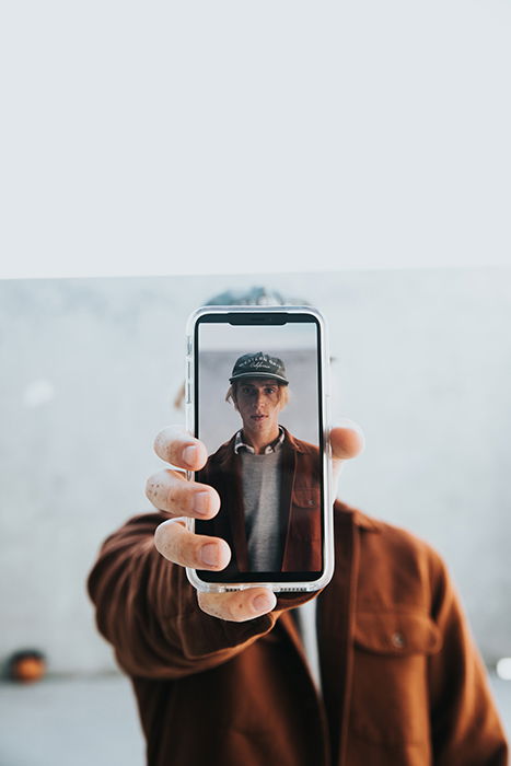 A man holding a camera phone with his self portrait on the screen 