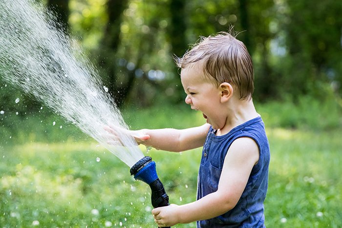 A small boy playing in the garden with a sprinkler 