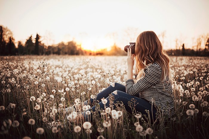 Girl in a field taking a photo of the landscape 