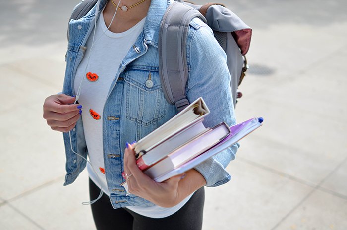 Girl with backpack holding a stack of books 