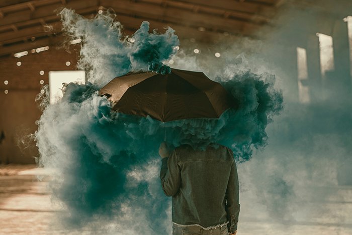 Surreal photo of a person standing with an umbrella with the use of a green smoke bomb