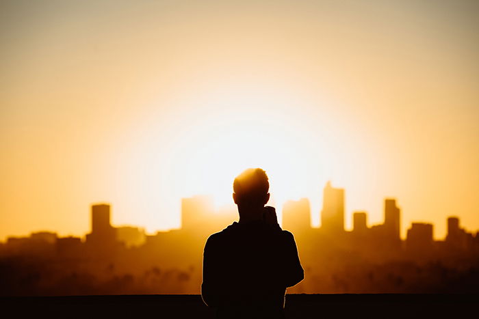 Photo of the silhouette of a man on top of a tall buinding at sunset