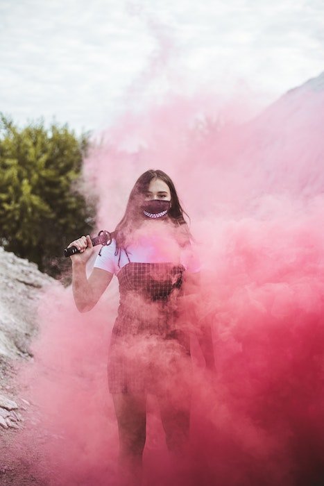 Garota de pé em uma bomba de fumaça rosa usando uma máscara como ideia para uma foto surreal