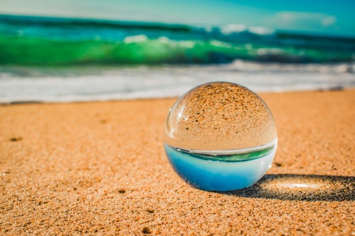a crystal ball lying on the sand of a beach, the image reflected inside