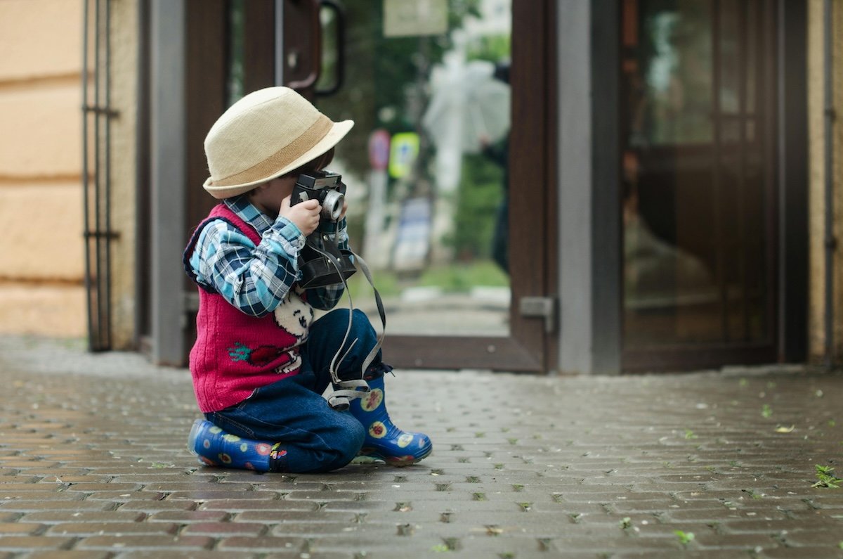 A child crouching with a camera on a sidewalk to take a picture to show photography for kids
