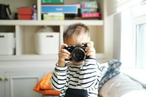 A boy holding up a camera to his face in a living room to show photography for kids