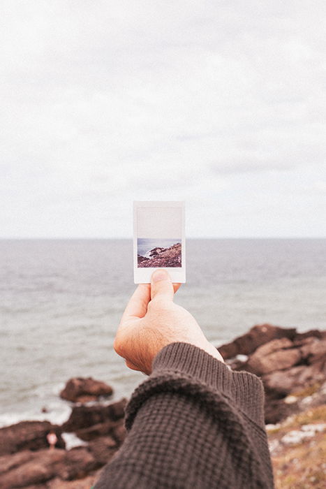 Photo of a hand holding a Polaroid picture of a beach