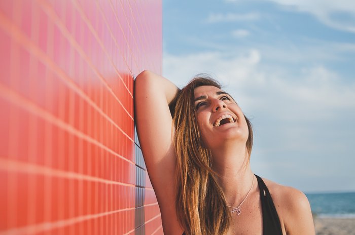 A woman laughing in the sunshine next to a red wall 