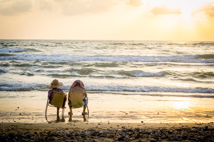 An elderly couple sitting right next to the sea in yellow camping chairs 