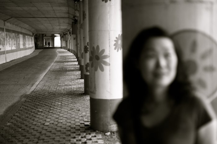 blurry black and white portrait of a girl standing against a stone column
