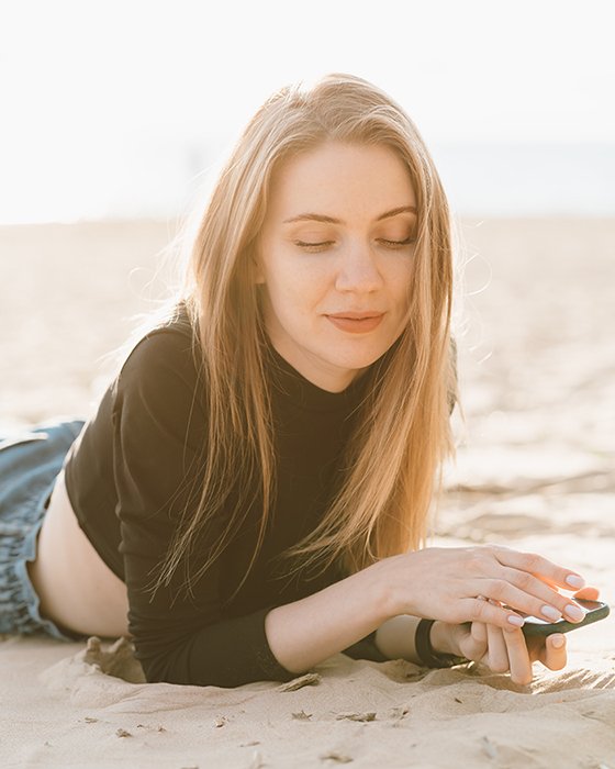 Young beautiful woman with long hair is relaxing on sandy beach in backlight.