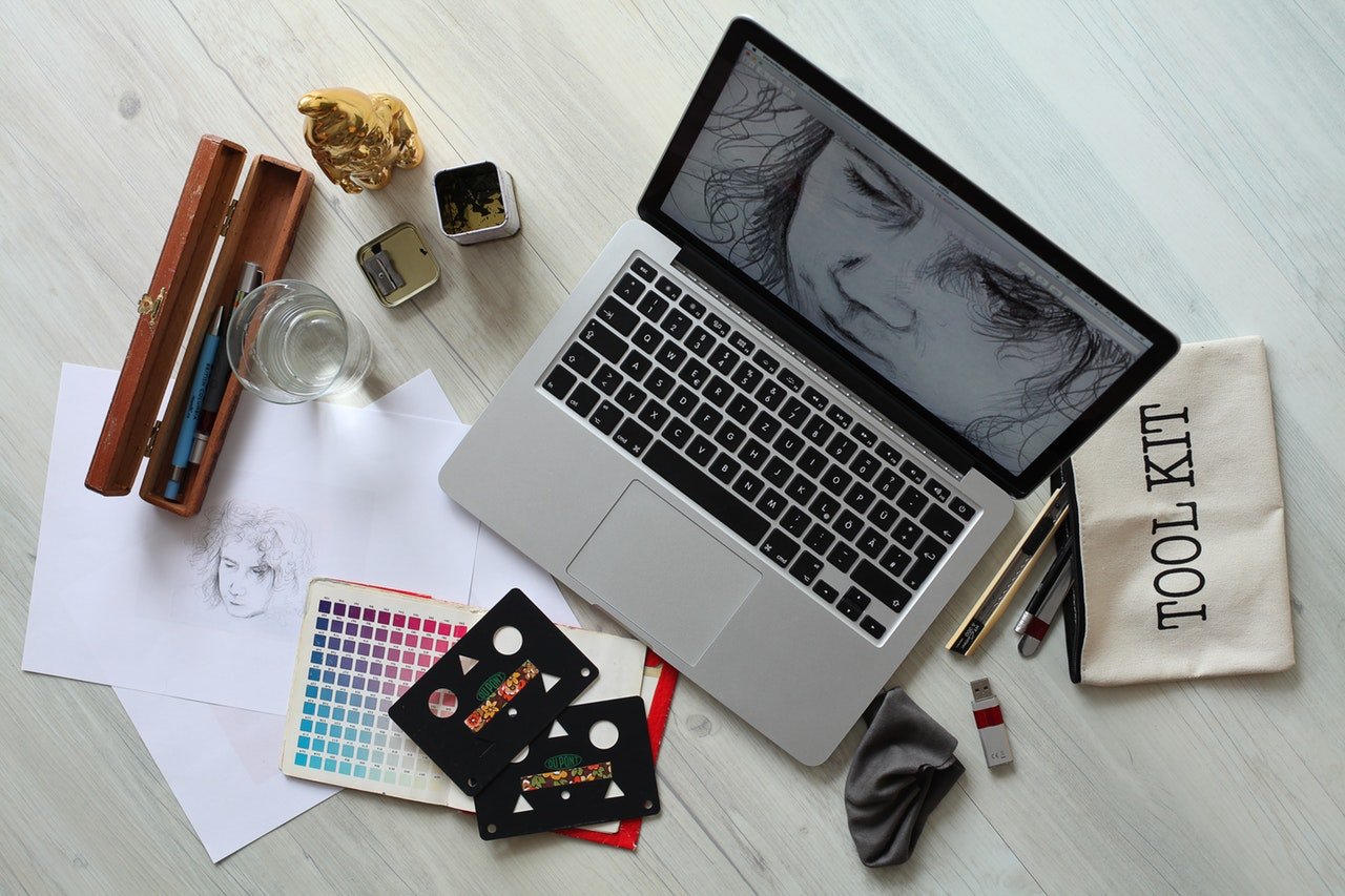 Overhead shot of a laptop with a face drawing on its screen and on a table with art supplies