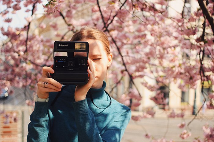a girl taking photos with a Polaroid camera under cherry blossom trees 