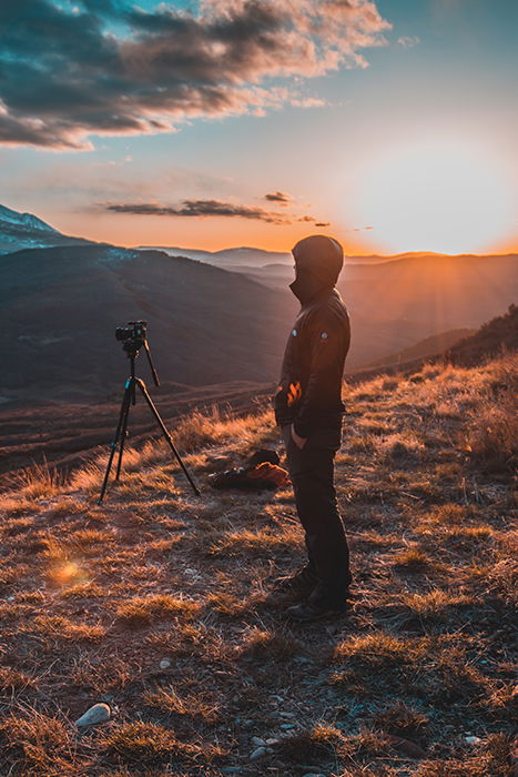 A man on a mountain with a tripod and camera 